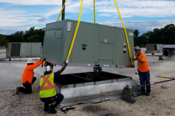 Four technicians wearing safety gear assisting with equipment delivery via crane