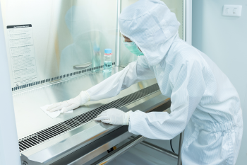 Technician wearing all white scrubs and medical gloves wiping down equipment in a critical environment facility